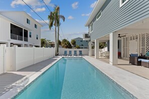 Ein Schwimmbecken mit Holzterrasse, Liegestühlen und einer überdachten Veranda.