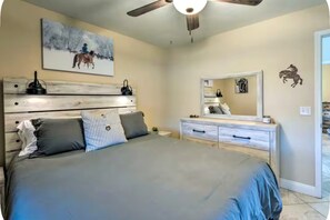 Ein Schlafzimmer mit einem Bett, einem Schminktisch, einem Deckenventilator, einem Gemälde und einem Spiegel.