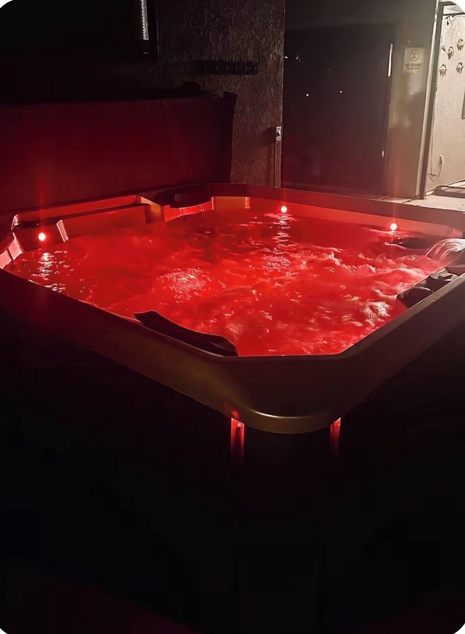 Un bain à remous éclairé d’une lumière rouge, entouré de murs sombres et doté d’une porte bien visible.