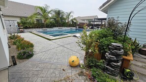 A backyard with a swimming pool, stone wall, and various plants.