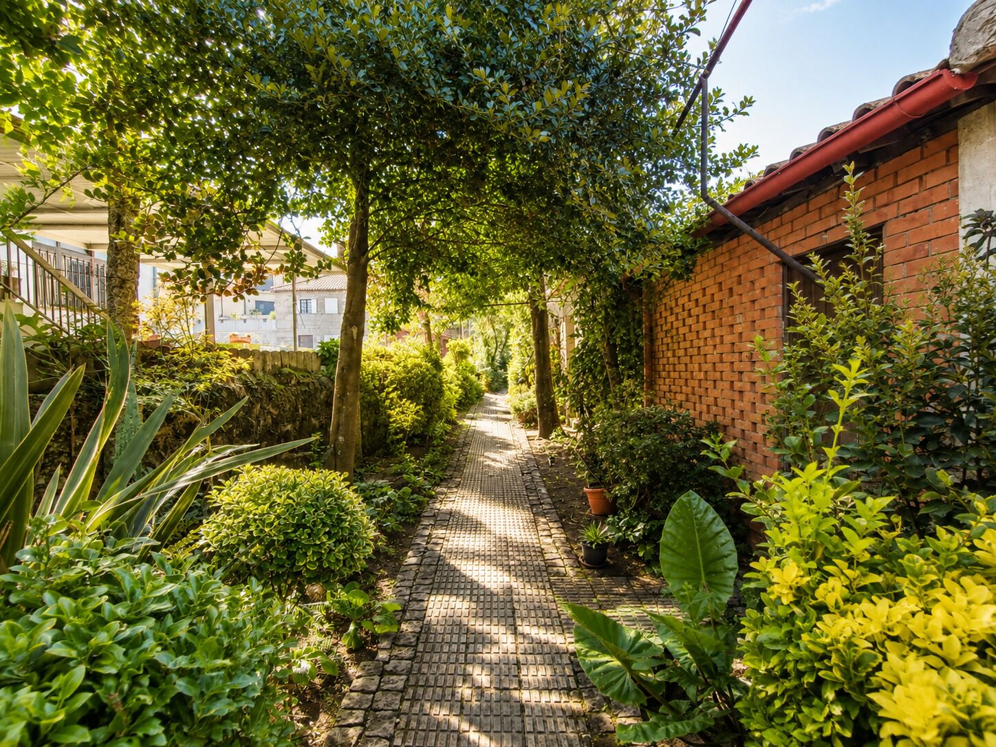 Un chemin de jardin bordé d’un côté par un mur de briques et de l’autre par un bâtiment.