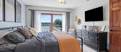 A bedroom with a bed, a dresser, a television, and a view of a body of water through a sliding door.