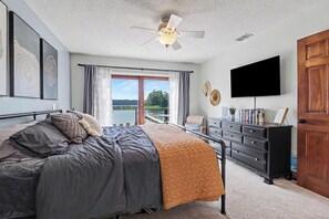 Een slaapkamer met een bed, een dressoir, een televisie en uitzicht op een waterpartij door een schuifdeur.