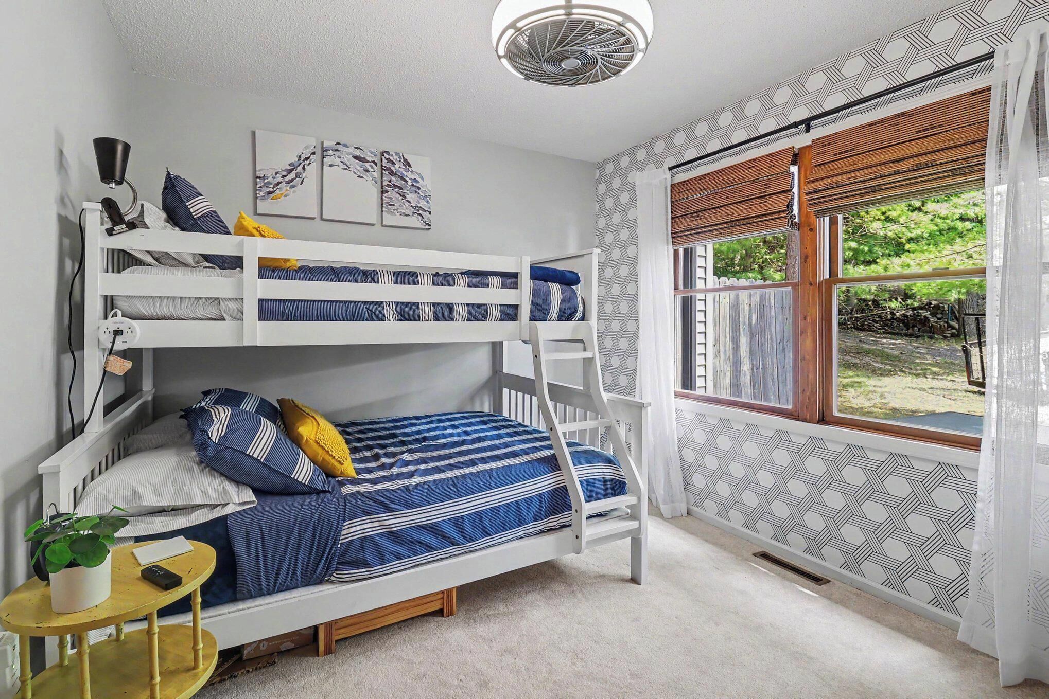 A bunk bed room with a window, a small table with a plant, and a ceiling fan.