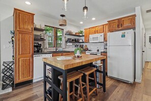 A modern kitchen with wooden cabinets, a central island with stools, a refrigerator, and pendant lighting. - Gun Lake Beachfront, Pet-Friendly Home w Dock (Free Soil)
