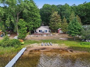 A lakeside cabin with a dock, surrounded by dense forest. - Gun Lake Beachfront, Pet-Friendly Home w Dock (Free Soil)