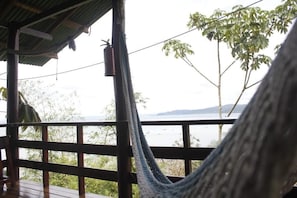 Una hamaca en una terraza de madera con vista a un cuerpo de agua, árboles y una lejana vista de tierra firme.