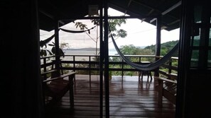 A wooden deck with a hammock, a bench, and a view of a natural landscape.