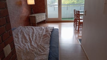 A bedroom with a bed, a dresser, a lamp, and a view of the outside.