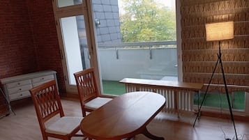 A room with a wooden table and chairs, a radiator, a bench, and a view of a balcony with a railing.