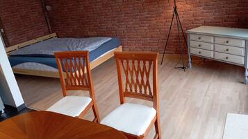 A room with a bed, two wooden chairs, a small table, a floor lamp, and a dresser.