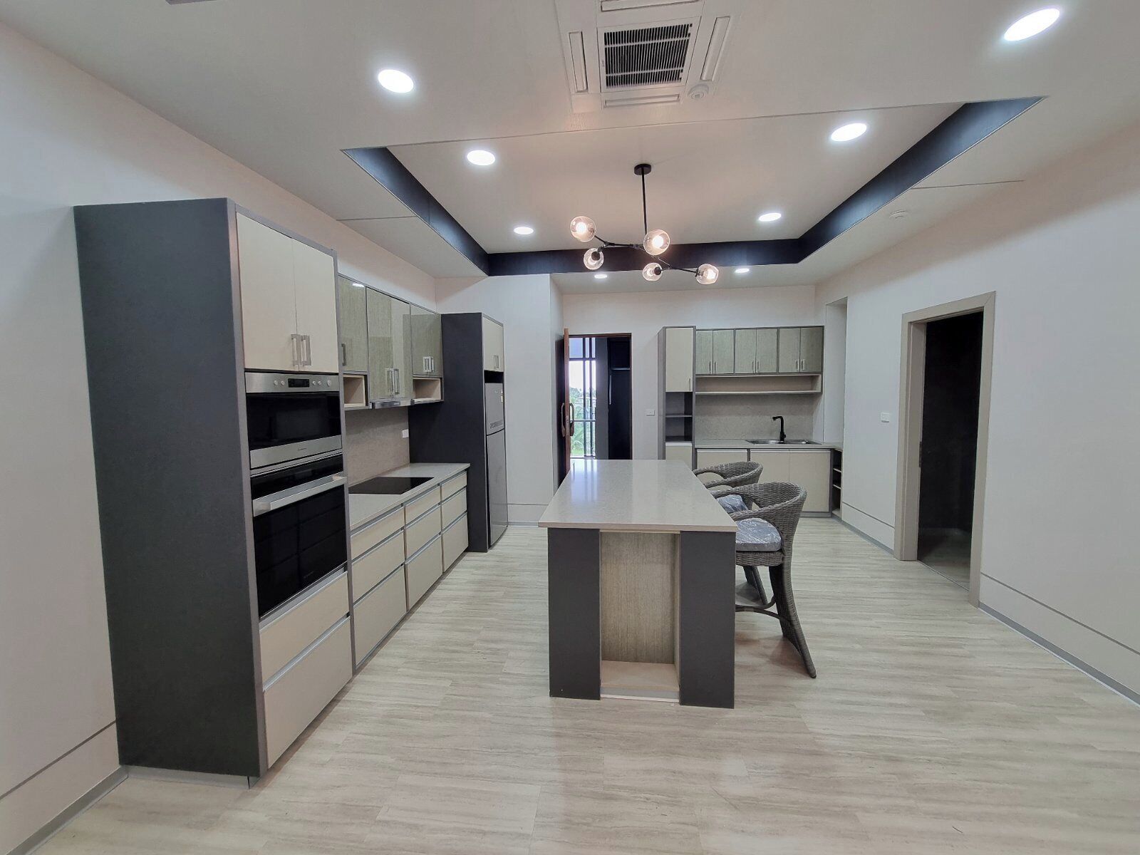 A modern kitchen with built-in appliances, a central island, and a dining area with wicker chairs.
