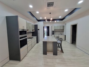 A modern kitchen with built-in appliances, a central island, and a dining area with wicker chairs.