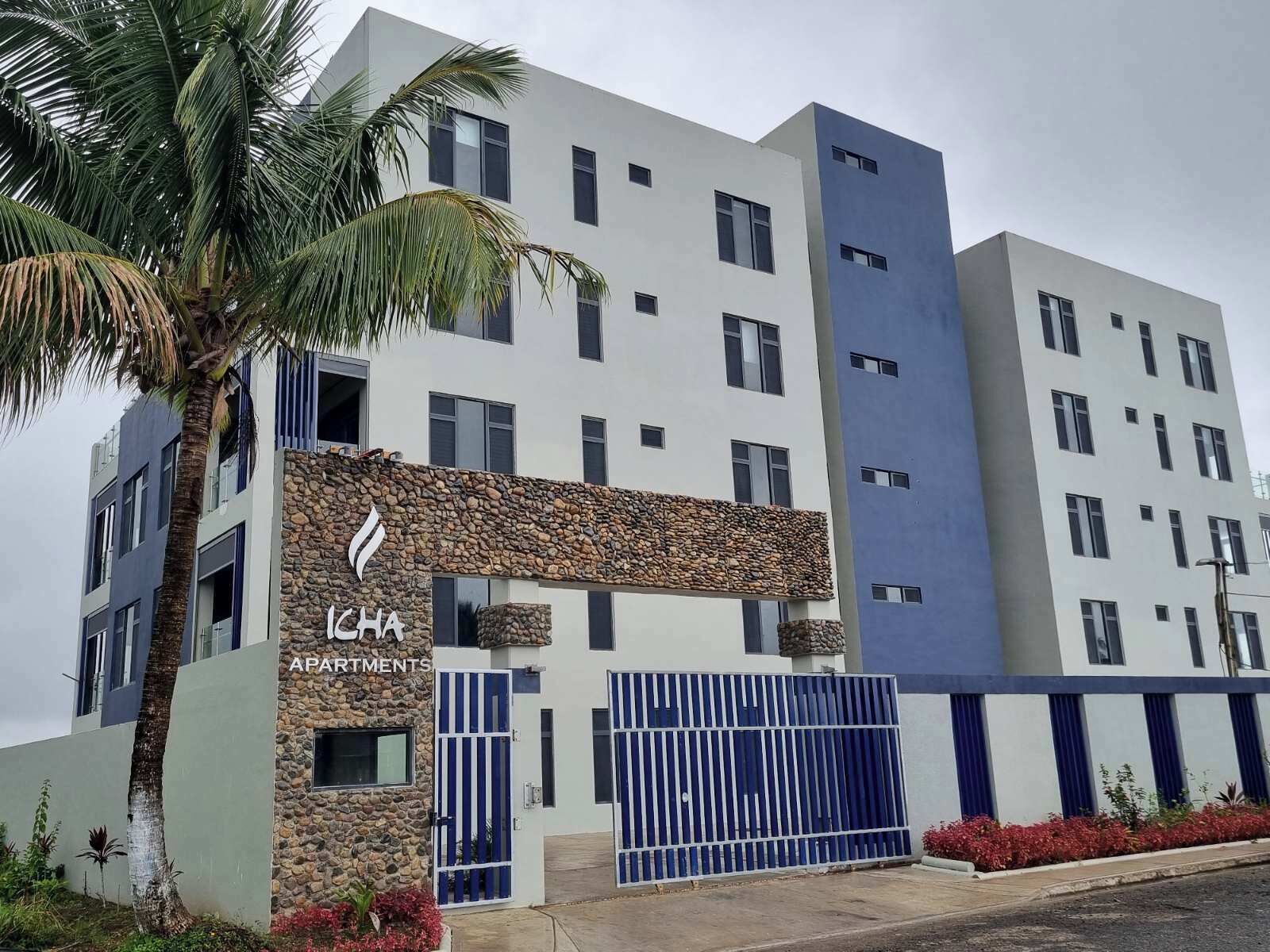 A multi-story building with a stone facade, a gated entrance, and a palm tree in the foreground.