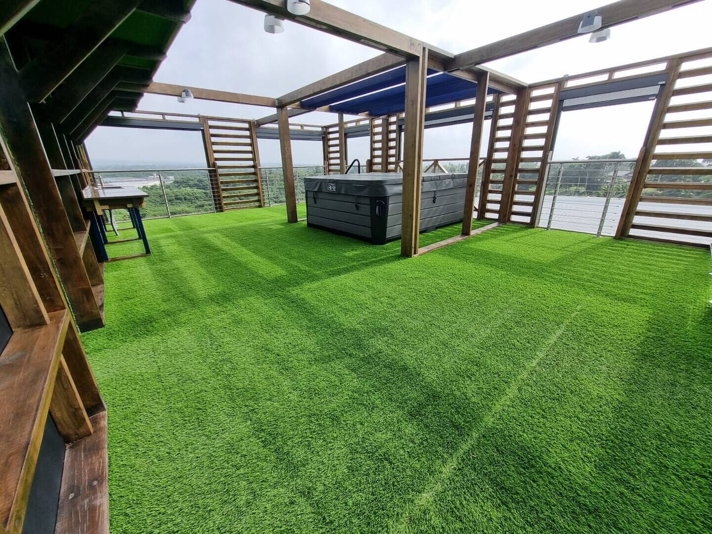 A rooftop terrace with artificial grass, a hot tub, and wooden railings.