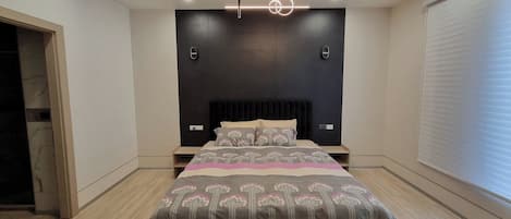 A modern bedroom with a large bed, a dark accent wall, and recessed ceiling lighting.