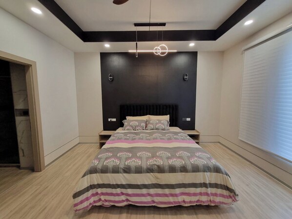 A modern bedroom with a large bed, a dark accent wall, and recessed ceiling lighting.