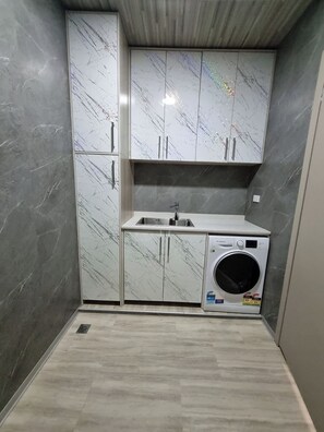 A compact kitchen with a built-in washing machine, a sink, and cabinets with a marble-like finish.