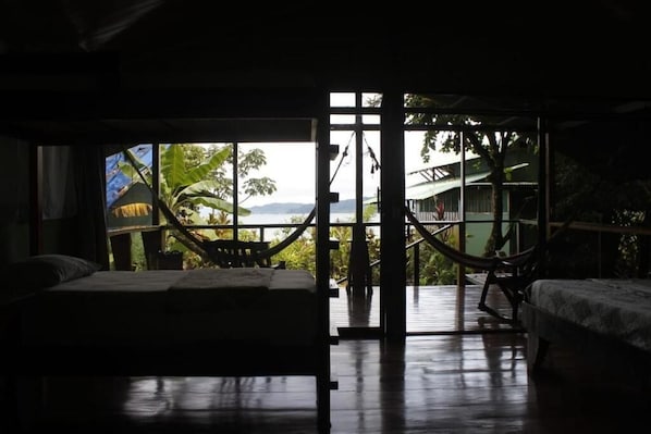 A room with a bed, a hammock, and a view of the outdoors.