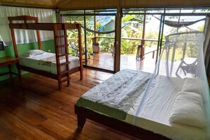 Una habitación con una cama litera, una cama individual y un balcón con una hamaca.