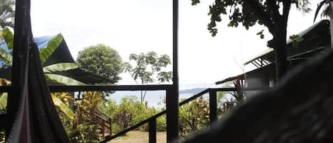 Un hamac dans une pièce donnant sur un jardin, avec un bâtiment visible au loin.