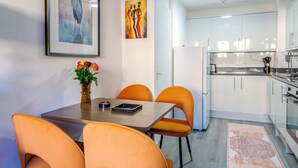 Une cuisine moderne avec des meubles blancs, une table à manger avec des chaises orange et un tableau accroché au mur.