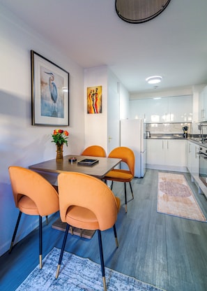 Una cocina moderna con armarios blancos, una mesa de comedor con sillas naranjas y un cuadro en la pared.
