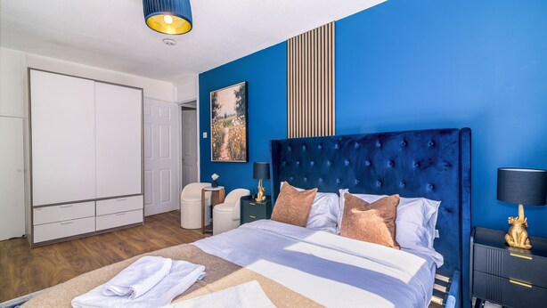 Une chambre à coucher avec un grand lit, une table de chevet, une lampe, un tableau au mur et une armoire.