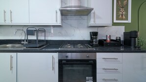 Une cuisine moderne avec des armoires blanches, un comptoir noir, une cuisinière en acier inoxydable, une machine à café et une œuvre d’art encadrée accrochée au mur.