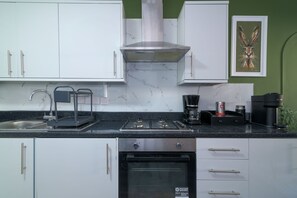 Una cocina moderna con armarios blancos, encimera negra, estufa de acero inoxidable, cafetera y una obra de arte enmarcada en la pared.