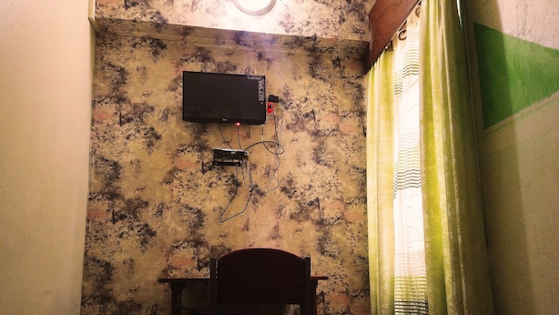 A room with a bed, a chair, a television mounted on the wall, and a window with curtains. - Hôtel Belle Vue Yaounde (Yaoundé)