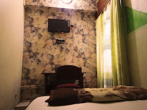 A room with a bed, a chair, a television mounted on the wall, and a window with curtains. - Hôtel Belle Vue Yaounde (Yaoundé)