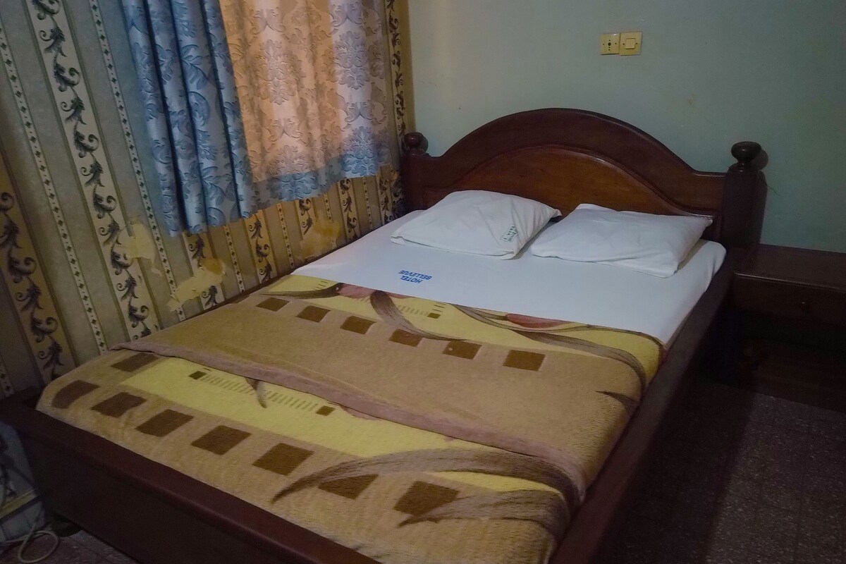 Una cama con cabecera de madera, almohadas blancas y colcha estampada.