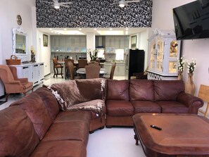 A living room with a brown leather sectional sofa, a dining area with chairs and a table, and a kitchen in the background. - Whale Hill Great View House (Puerto Peñasco)