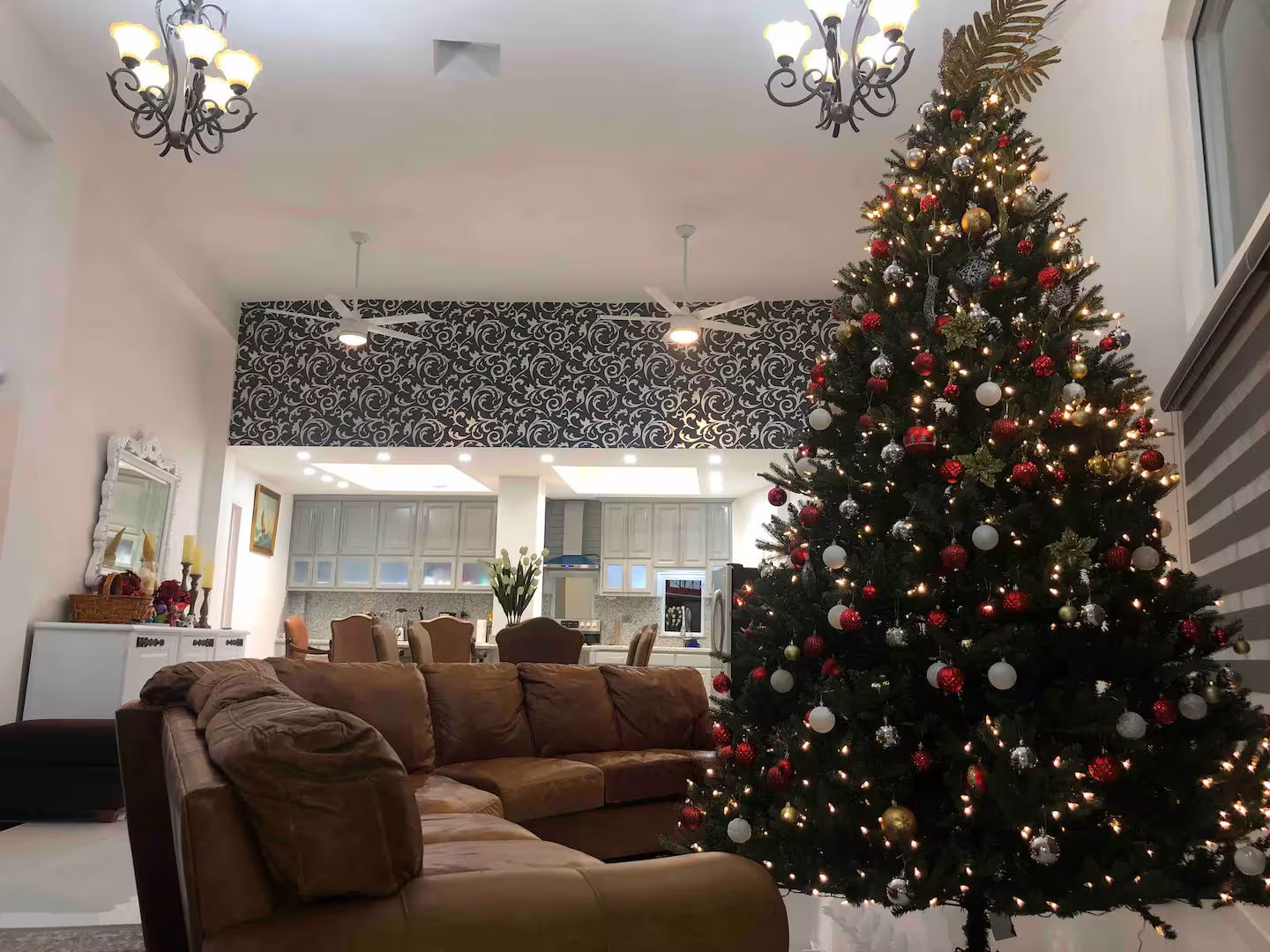 En stue med et stort juletræ, en brun lædersofa og et mønstret loft.