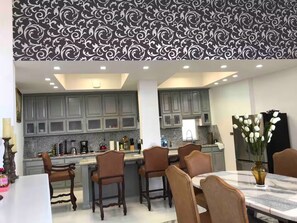 A modern kitchen with grey cabinets, a central island, and a dining area with a marble table. - Whale Hill Great View House (Puerto Peñasco)
