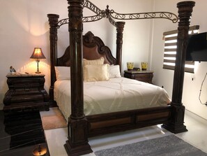 A four-poster bed with a dark finish, a bedside table with a lamp, and a flat-screen TV mounted on the wall. - Whale Hill Great View House (Puerto Peñasco)