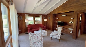 A room with a red sofa, two floral armchairs, a white coffee table, and a television on a wooden shelf.