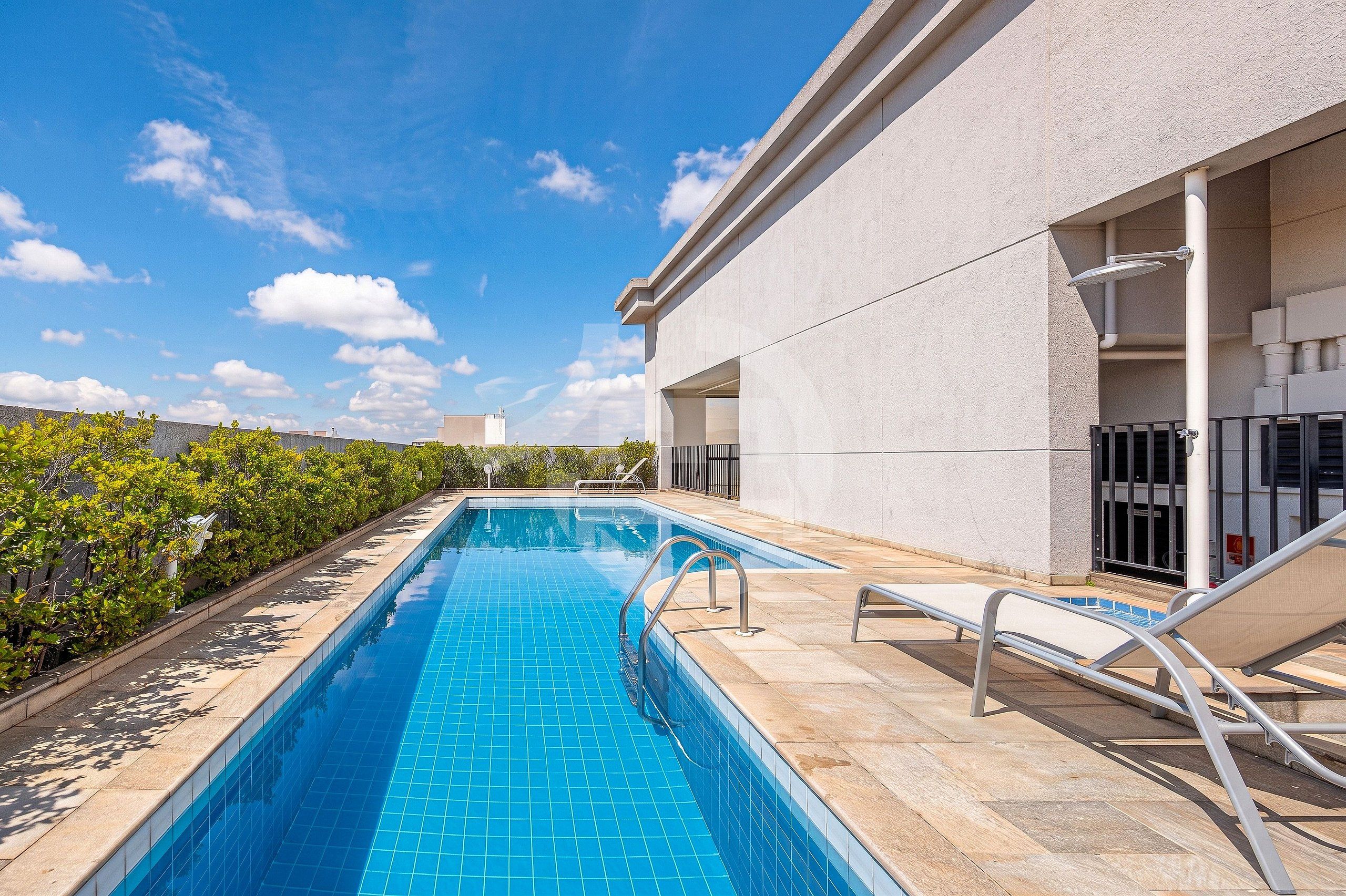 A swimming pool with a tiled edge, a metal handrail, and a lounge chair.