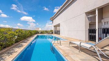 A swimming pool with a tiled edge, a metal handrail, and a lounge chair.