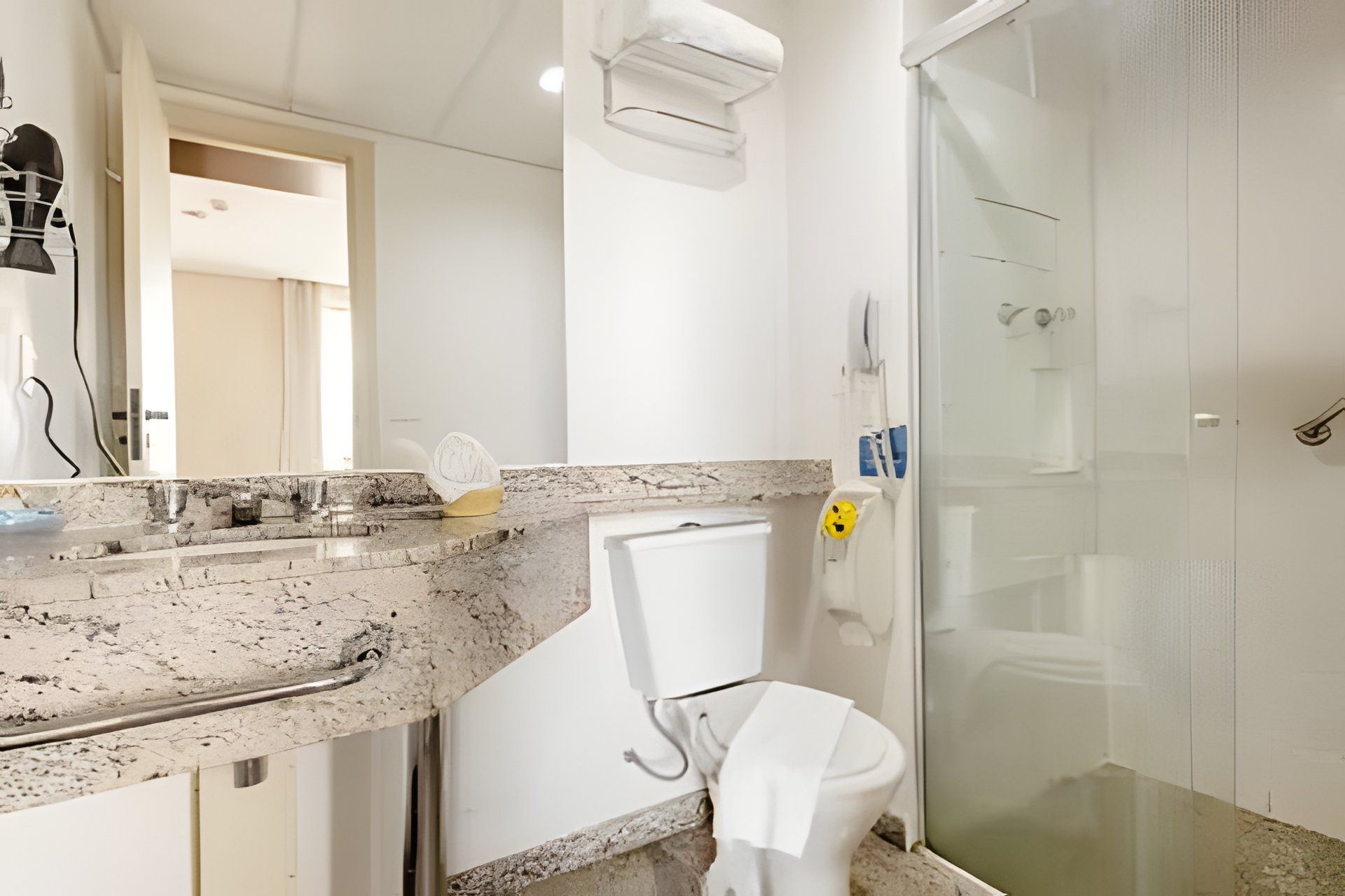 Un baño con encimera de granito, un inodoro blanco, cabina de ducha de vidrio y una toalla colgada en la pared.
