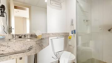 Un baño con encimera de granito, un inodoro blanco, cabina de ducha de vidrio y una toalla colgada en la pared.