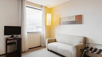Habitación de hotel moderna con sofá, televisor sobre un soporte, ventana con cortinas y un cuadro en la pared.