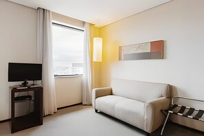 A modern hotel room with a sofa, a TV on a stand, a window with curtains, and a painting on the wall. - Osasco Trade Fundação (Osasco)