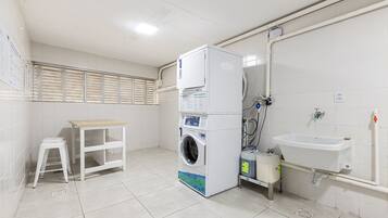 Un cuarto de lavandería con lavadora, pileta y un taburete.