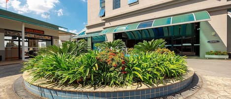 Entrada de hotel con una jardinera de azulejos, un toldo verde y un letrero que dice 'GRÃO ESPREVO'.
