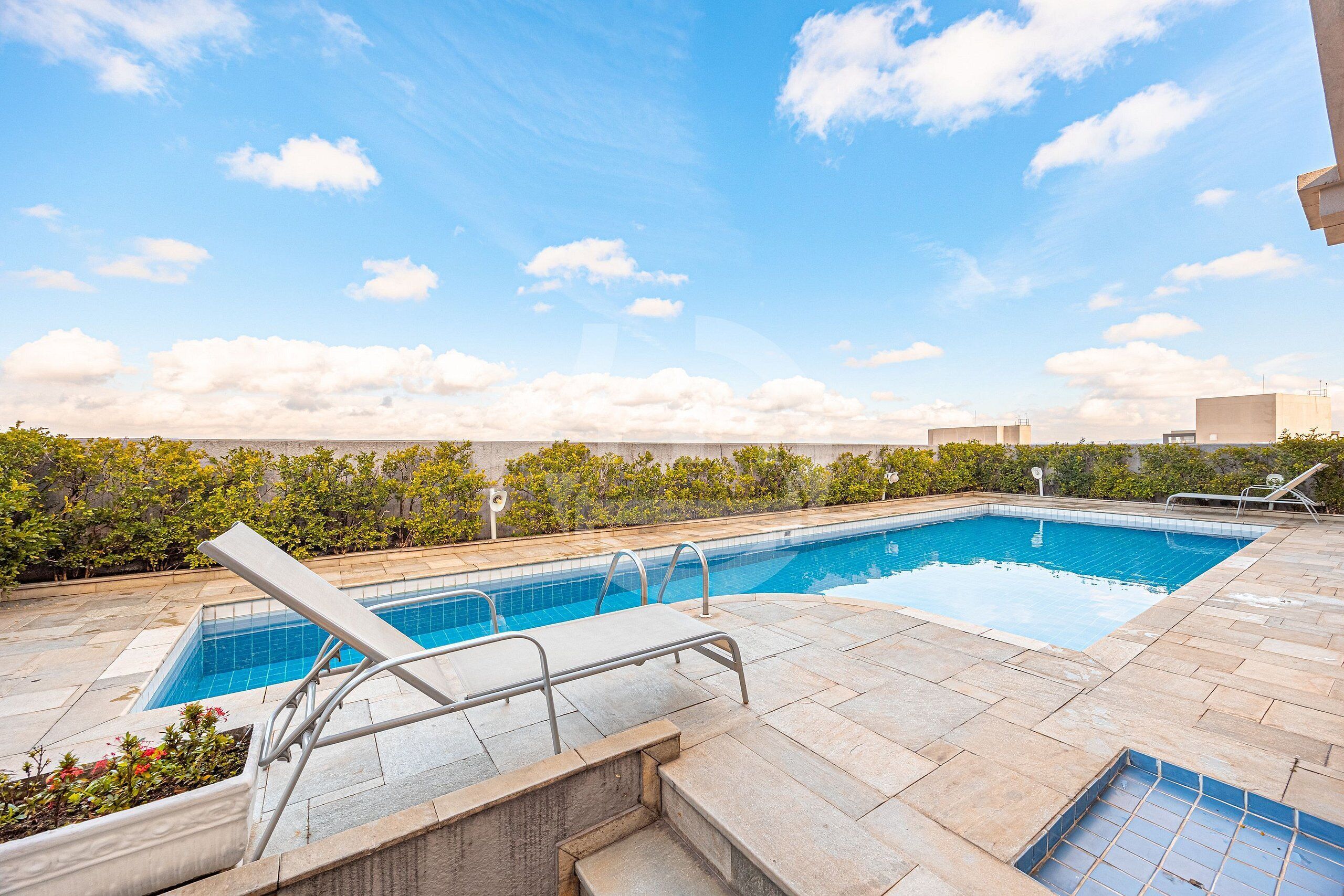 A rooftop swimming pool with clear blue water, surrounded by stone tiles and greenery.
