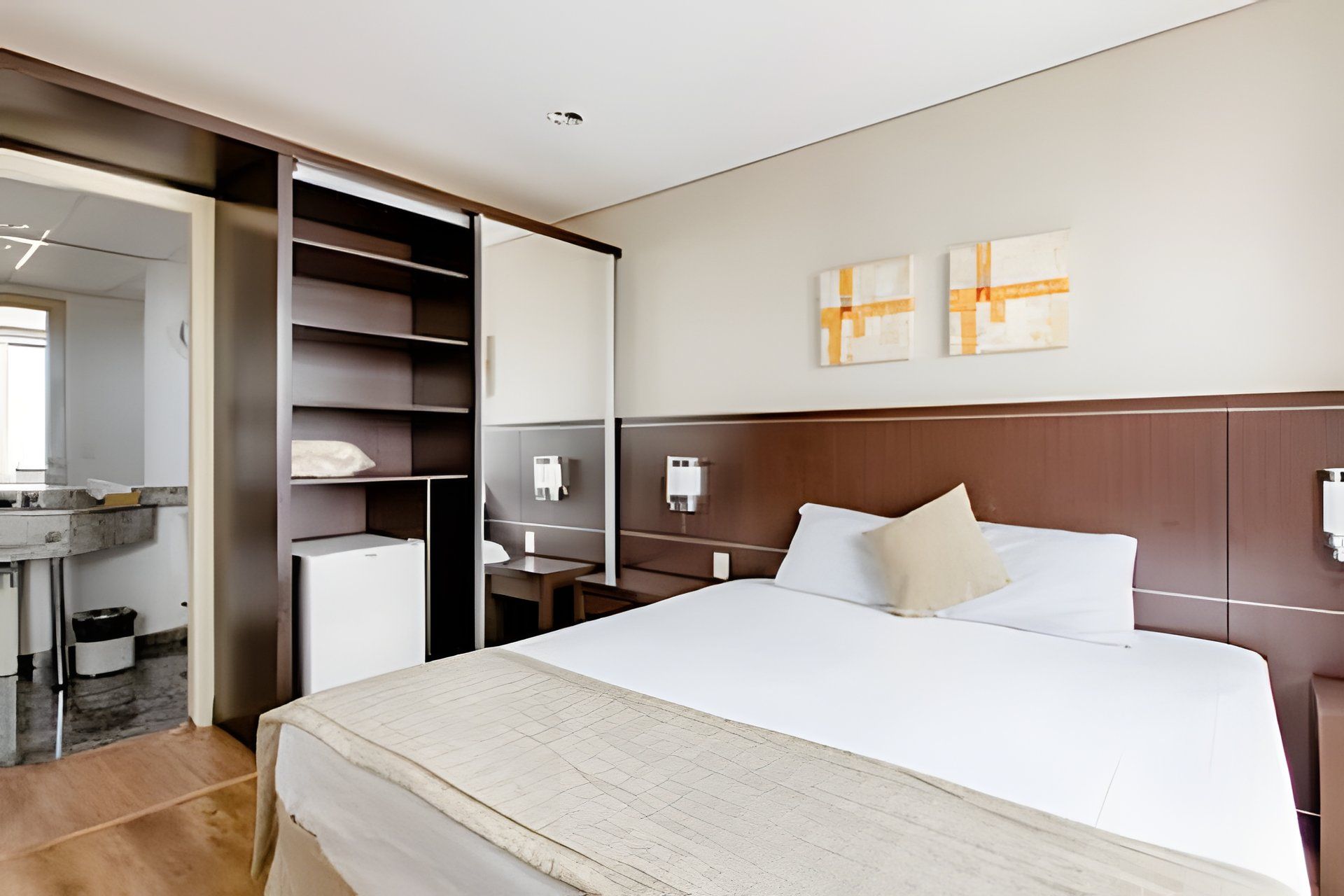 Ein Hotelzimmer mit einem Bett, einem Schreibtisch, einem Stuhl, einem Kleiderschrank und einer kleinen Kühlbox.