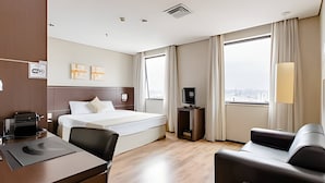 A hotel room with a bed, a desk with a printer, a TV, and a view of the city through large windows. - Osasco Trade Fundação (Osasco)