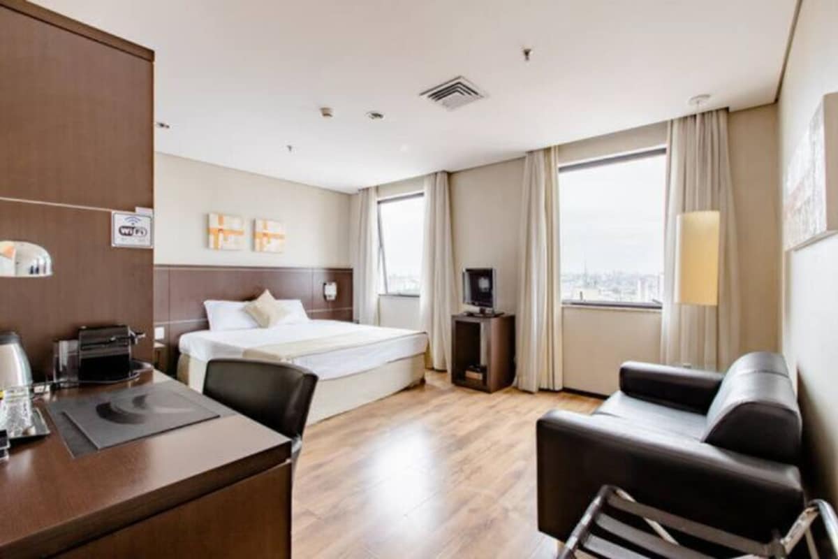 A hotel room with a bed, a desk, a chair, a TV, and a window with curtains.